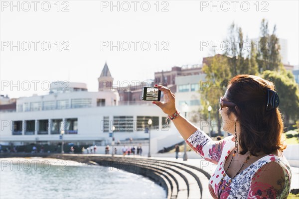 Hispanic woman taking cell phone photograph of waterfront
