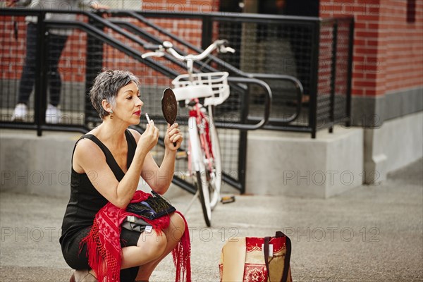 Older Caucasian woman applying makeup in mirror on sidewalk