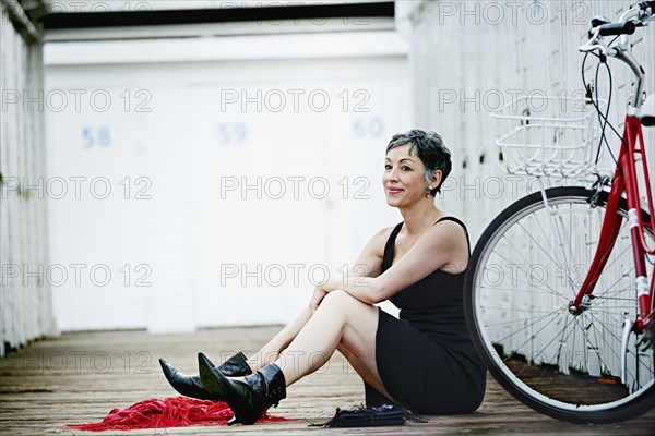 Older Caucasian woman sitting with bicycle on wooden dock