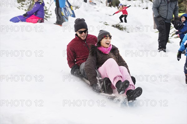 Hispanic couple sledding on snowy hillside