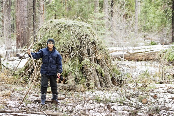 Hispanic boy building hut from branches in forest