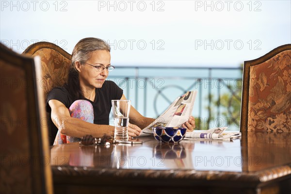 Hispanic woman reading newspaper at table