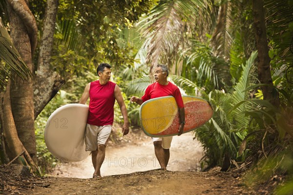 Hispanic men carrying surfboards on jungle trail