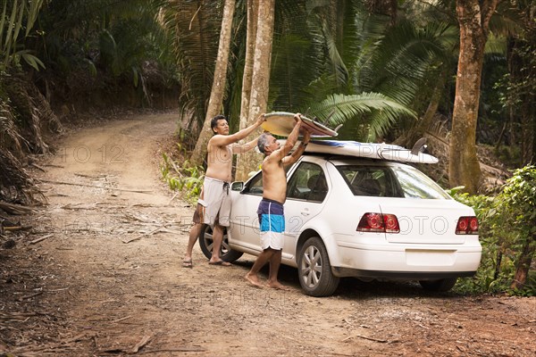 Hispanic men placing surfboards on roof of car in jungle