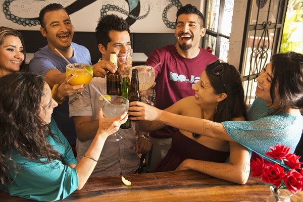 Hispanic friends toasting with drinks at bar