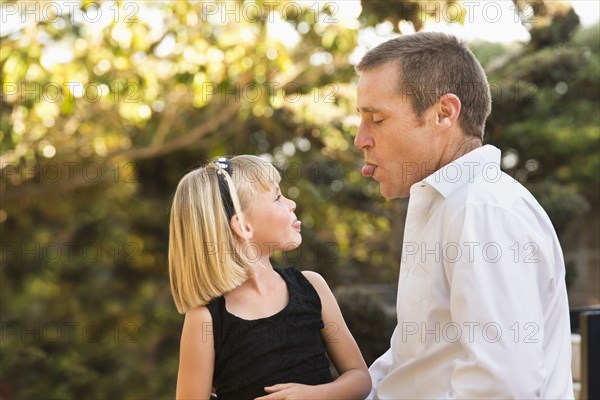 Caucasian father and daughter sticking out tongues