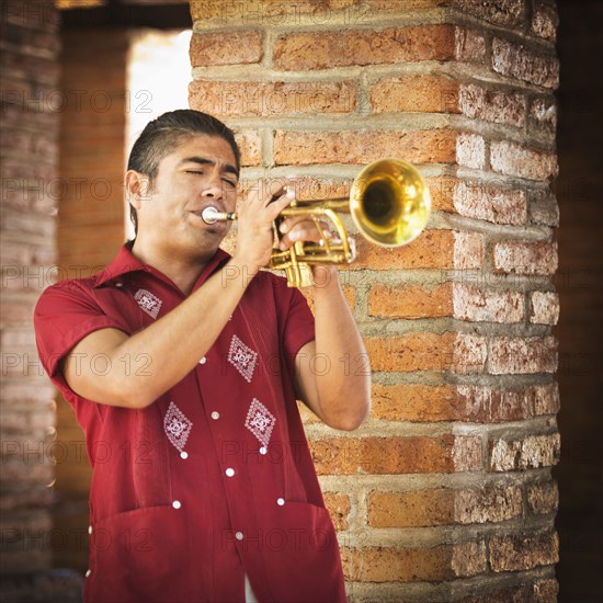 Hispanic musicians playing trumpet near brick wall