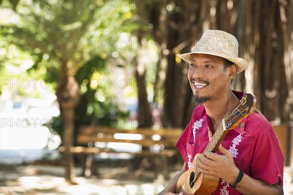 Hispanic musician playing ukulele in park