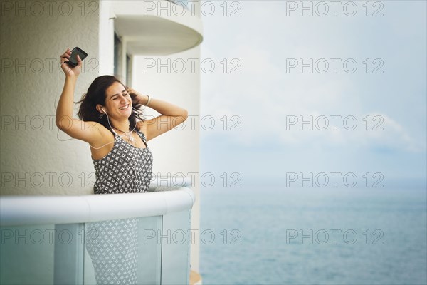 Hispanic woman dancing near ocean on hotel balcony
