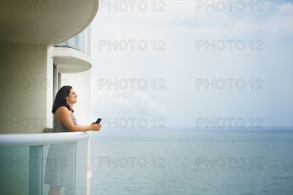 Hispanic woman admiring ocean from hotel balcony