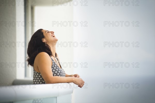 Hispanic woman laughing near ocean hotel balcony