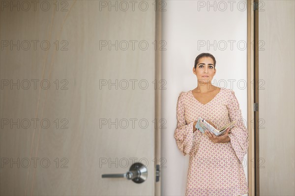 Worried Hispanic woman peering through door crack