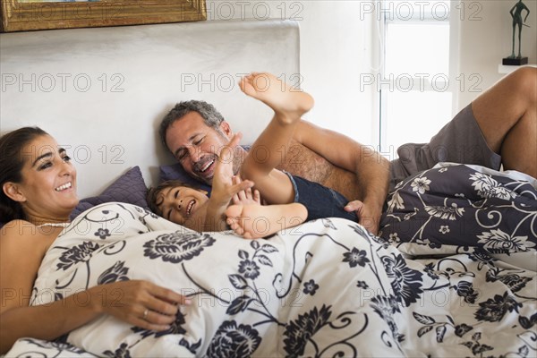 Hispanic father tickling son in bed