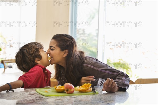 Hispanic mother and son eating fruit in kitchen