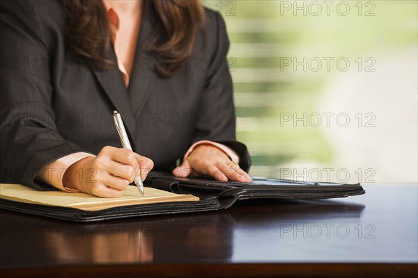 Hispanic businesswoman writing notes at desk