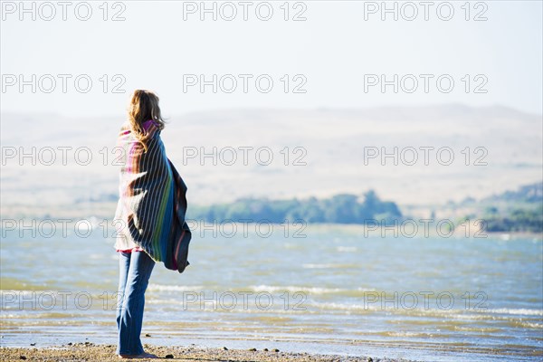 Caucasian woman wrapped in blanket on beach