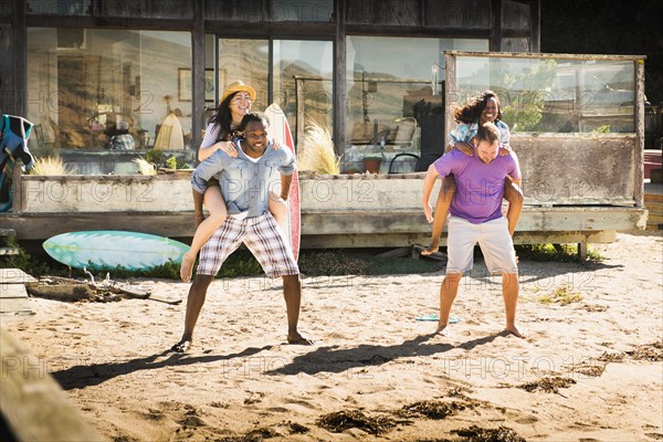 Men carrying girlfriends piggyback in sand