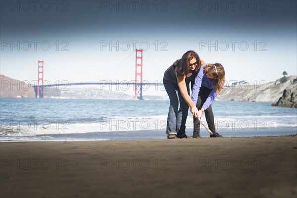 Mother and daughter drawing in sand on beach