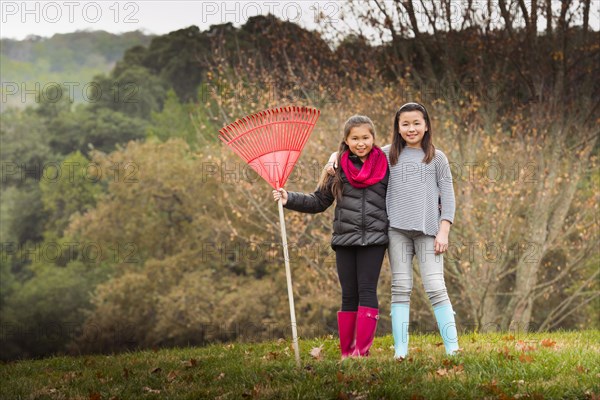 Mixed race sisters raking autumn leaves on lawn