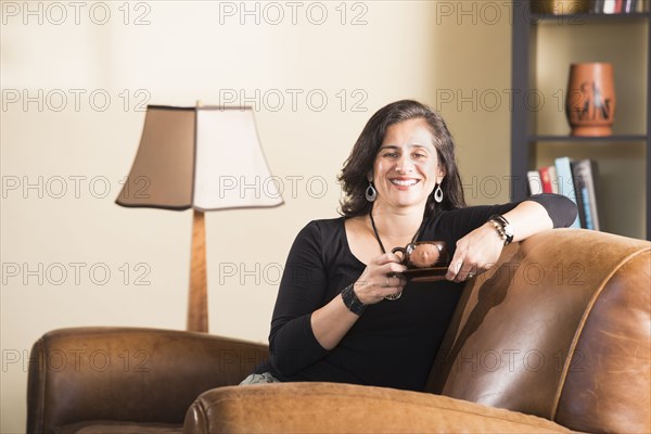 Hispanic woman sitting in armchair drinking coffee