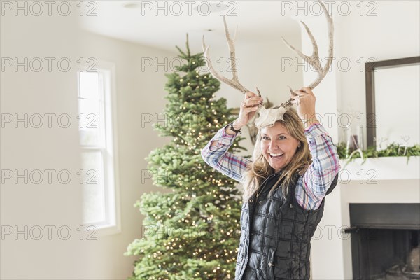 Caucasian woman holding antlers to head near Christmas tree