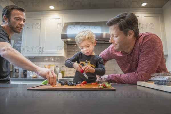 Caucasian fathers watching son cut berries in kitchen