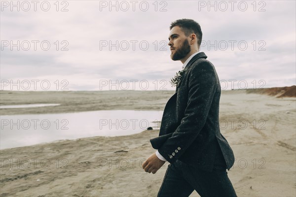 Caucasian groom walking on beach