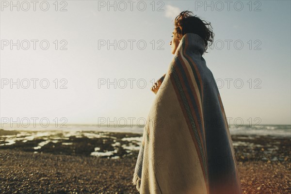 Caucasian woman wrapped in blanket at beach