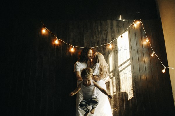 Caucasian couple hugging near boy under string lights