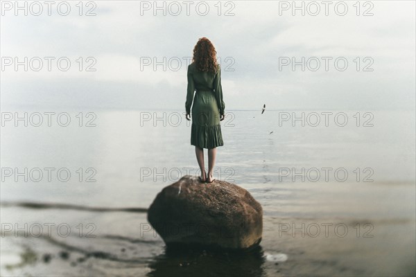 Caucasian woman wearing dress standing on rock at beach