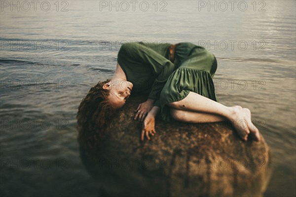 Caucasian woman wearing dress laying on rock at beach