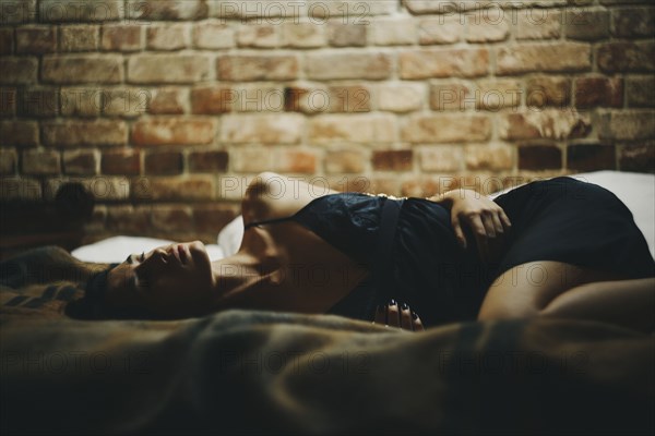 Caucasian woman laying on bed near brick wall