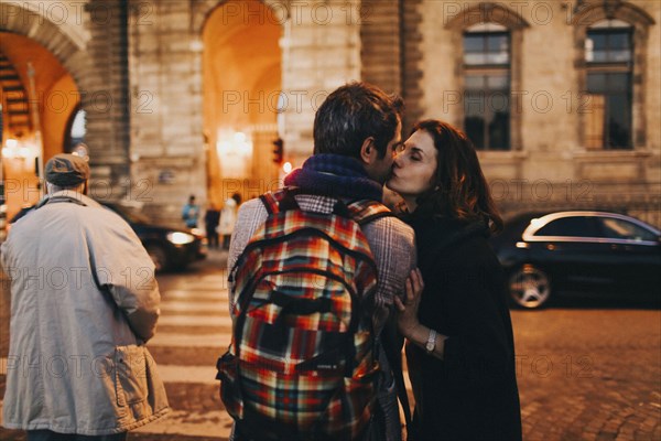 Caucasian woman kissing man on cheek in city at night