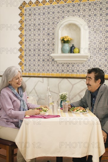 Smiling older couple eating salad and laughing in restaurant