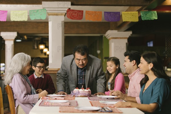 Older man blowing out candles on birthday cake in restaurant