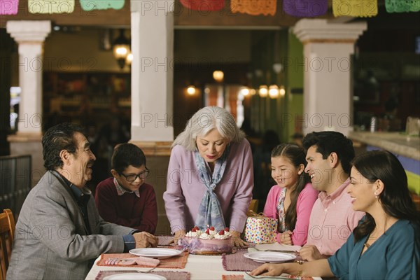 Older woman blowing out candles on birthday cake in restaurant