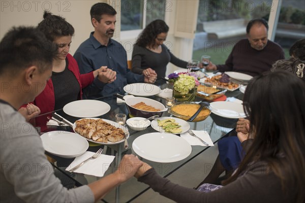 Multi-generation family praying before eating meal