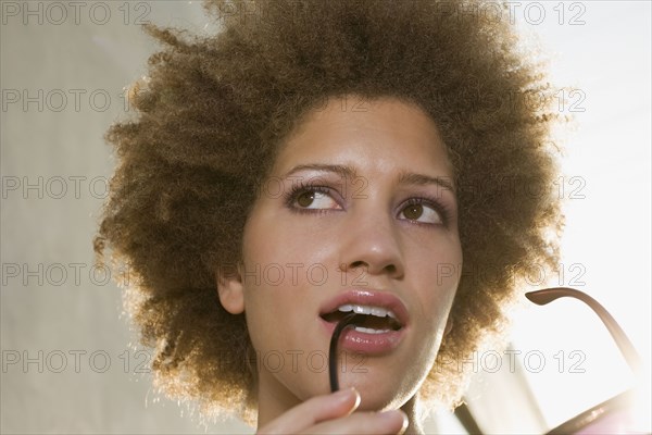 Mixed race woman biting on sunglasses