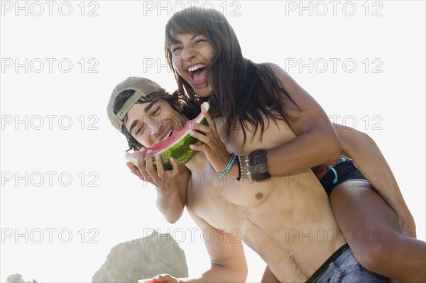 Woman eating watermelon getting piggy back ride from boyfriend