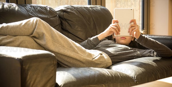 Girl laying on sofa reading digital tablet
