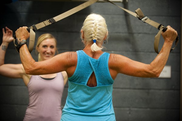 Trainer assisting older woman working out in gymnasium