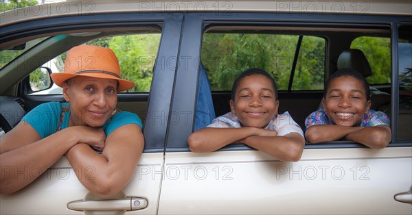 Portrait of mother and twin sons leaning on car windows