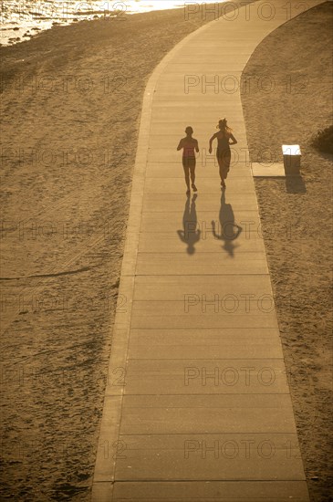 Mixed Race mother and daughter running on path at beach