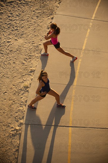 Mixed Race mother and daughter stretching on path at beach