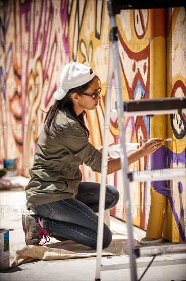 Woman kneeling on tarp painting mural on wall