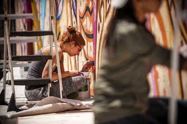 Women sitting on tarp painting mural on wall