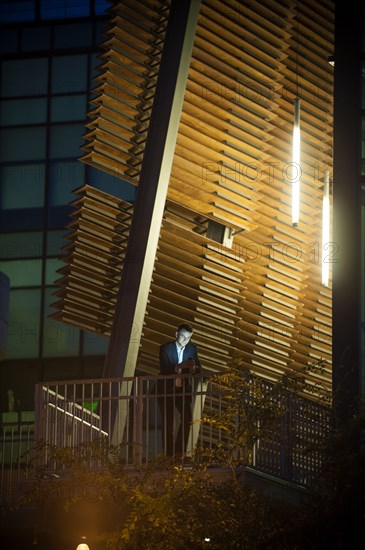 Businessman on balcony texting on cell phone at night