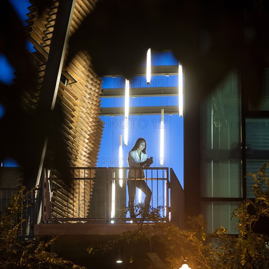 Businesswoman on balcony texting on cell phone at night