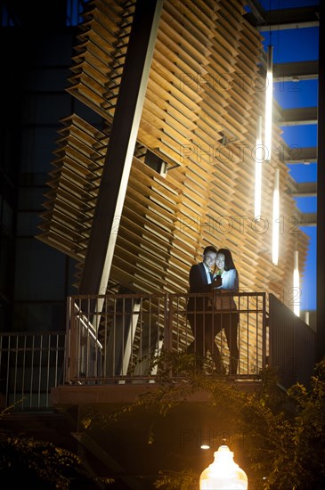 Couple standing on balcony posing for cell phone selfie at night