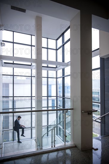 Hispanic businessman sitting on staircase railing near window